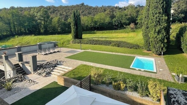 Ein Garten mit Swimmingpool, einer Terrasse und Blick auf einen bewaldeten Hügel.