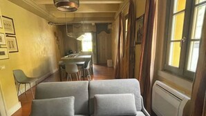 A modern living room with a grey sofa, a dining area with chairs, and a kitchen in the background. - Villa Valle Franciacorta - Yellow Apartment with Pool, Garden and Solarium (Rodengo-Saiano)