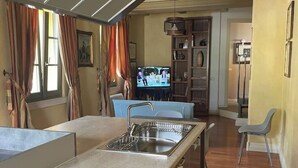 Eine kleine Küche mit Spüle, ein Essbereich mit blauem Stuhl und ein Fernseher im Hintergrund.