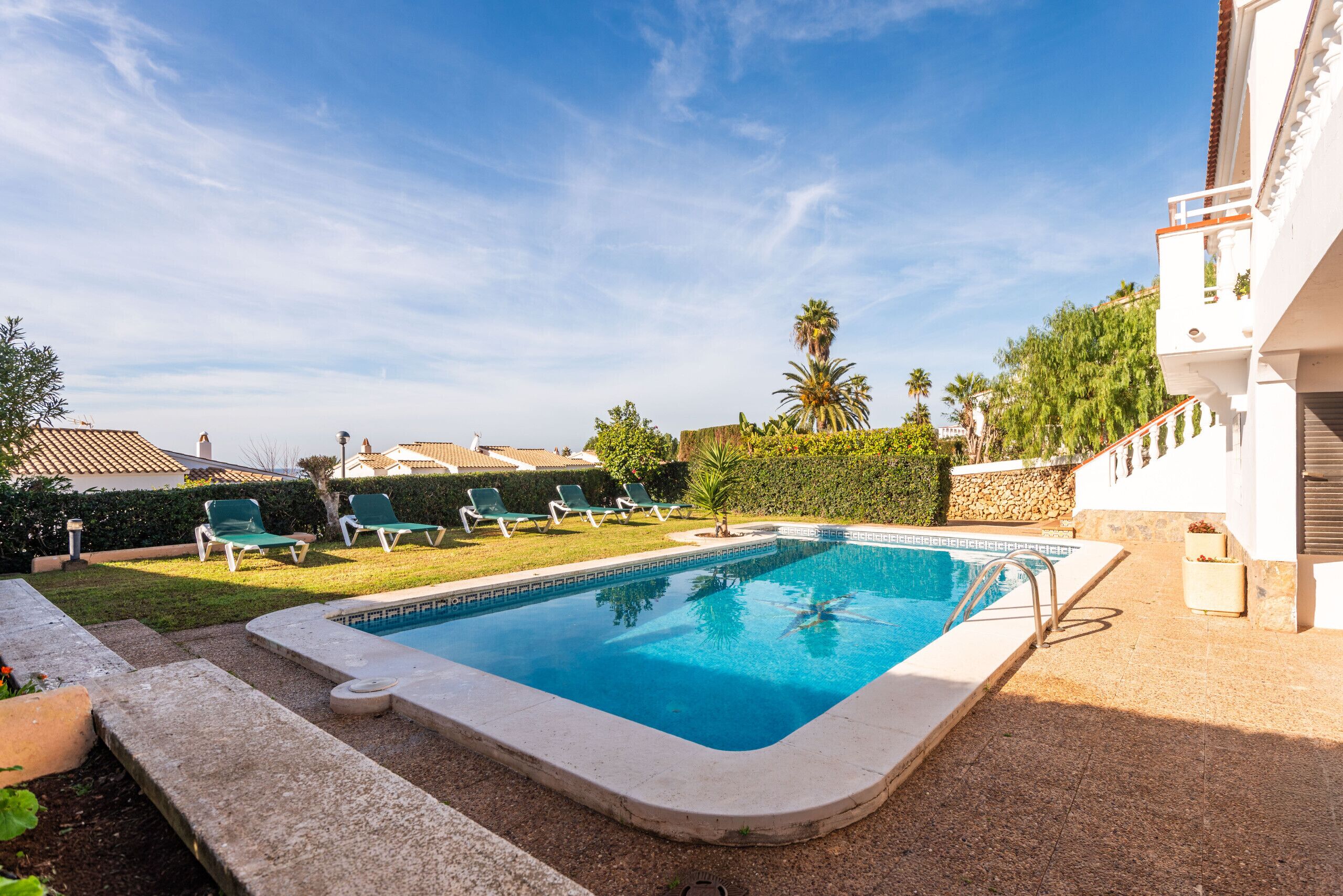 A swimming pool with a tiled deck, surrounded by lounge chairs and a stone wall.