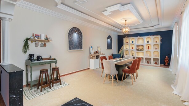 Un área de comedor con una mesa y sillas, una estación de café, y una estantería decorativa con varios objetos.