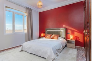 Ein Schlafzimmer mit einem großen Bett, zwei Nachttischen mit Lampen, einem Kleiderschrank und einem Fenster mit Vorhängen.