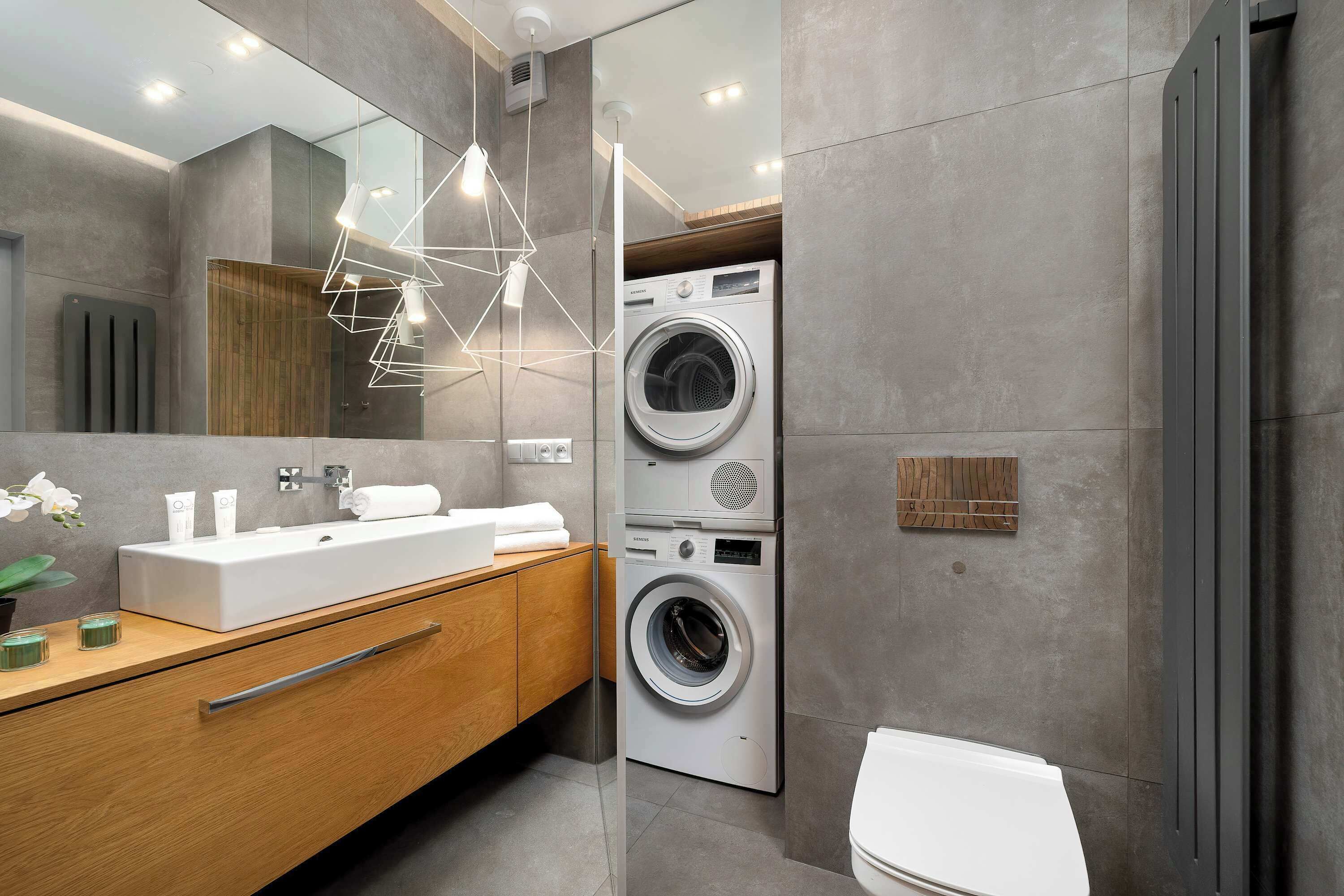 A modern bathroom with a large mirror, a wooden vanity, a built-in washing machine, and a toilet.