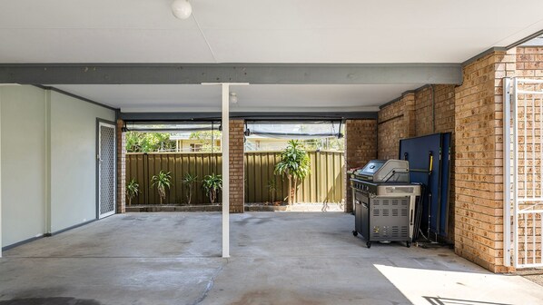 A covered outdoor area with a barbecue grill, a metal fence, and a brick wall.