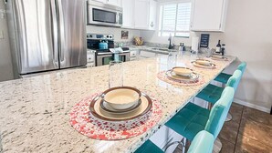 Una cocina moderna con electrodomésticos de acero inoxidable, encimera de granito y taburetes de bar color turquesa.