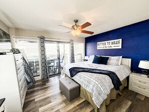 Un dormitorio con cama, ventilador de techo, mesita de noche, cómoda y ventana con cortinas.