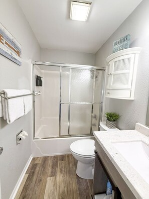 Un baño con cabina de ducha de vidrio, inodoro, lavabo con encimera blanca y armario con diseño perforado.