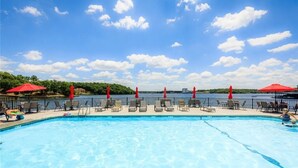 Una piscina con sillas de descanso y sombrillas rojas, con vista a una extensión de agua.