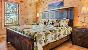 Quarto de cabana de madeira com uma cama, uma mesinha de cabeceira, um abajur e uma janela com persianas.