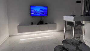 A modern living room with a flat-screen TV mounted on a wall, a white console table, and two marble-topped stools.