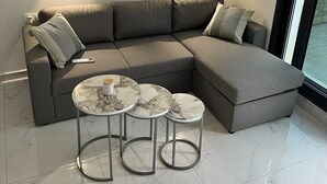 A modern living room with a grey sectional sofa, three marble-topped side tables, and two wall-mounted lights.