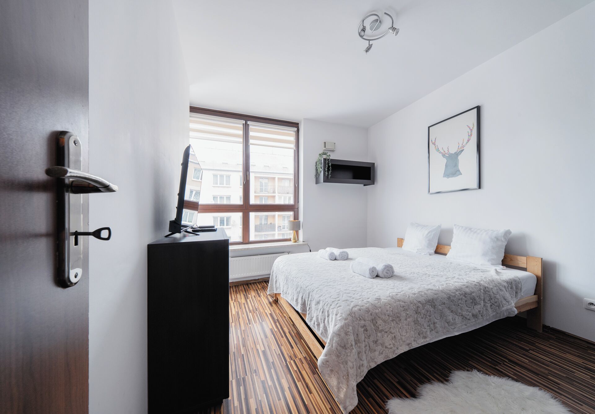 Une chambre à coucher avec un lit, un bureau avec un ordinateur, une fenêtre et une étagère fixée au mur.