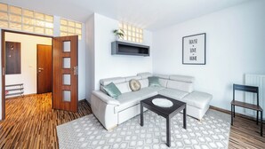 A modern living room with a sectional sofa, a coffee table, and a wall-mounted shelf. - RentPlanet - Kazimierza Wielkiego (Poznań)
