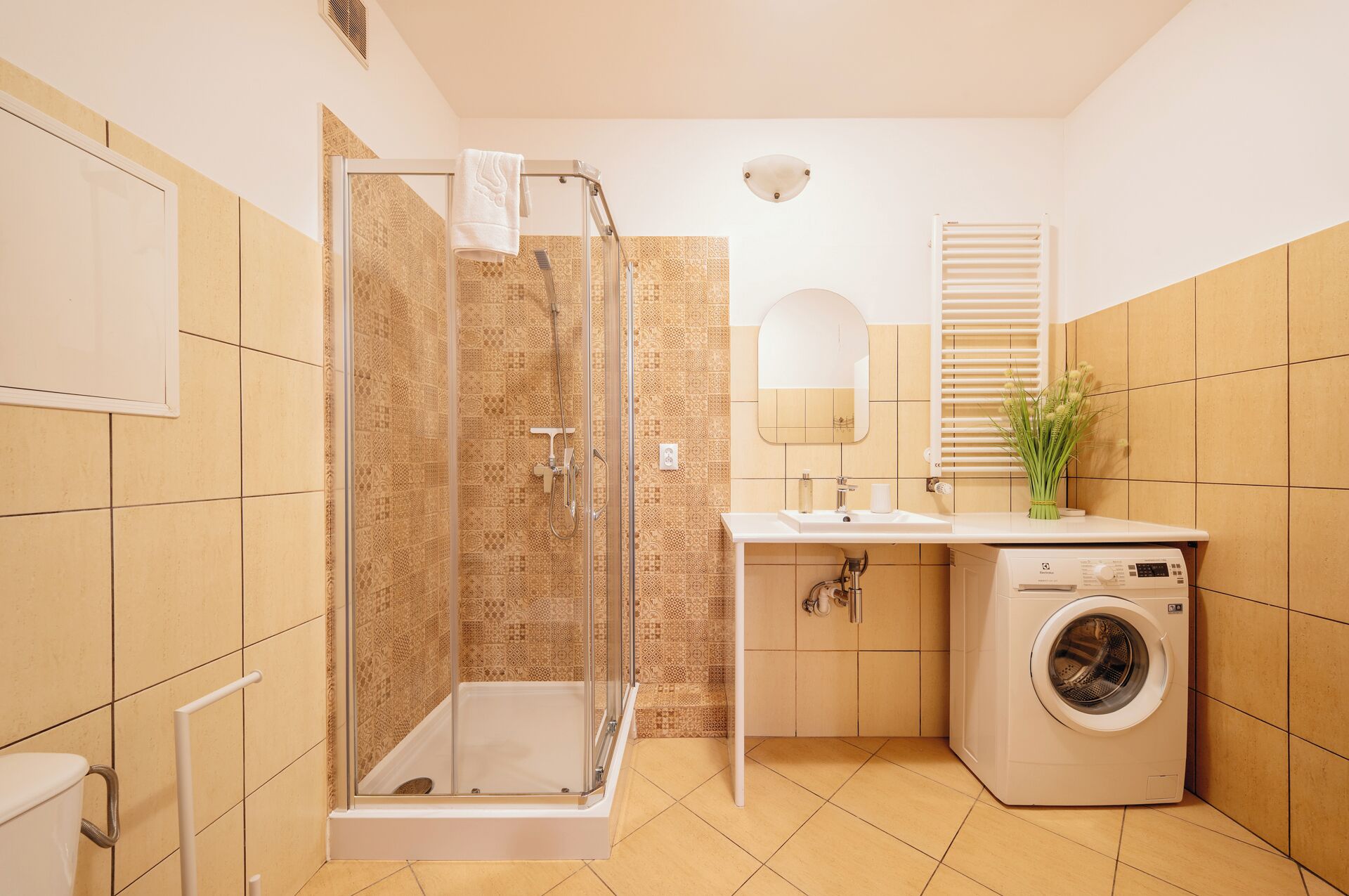 A bathroom with a shower, sink, mirror, and washing machine.