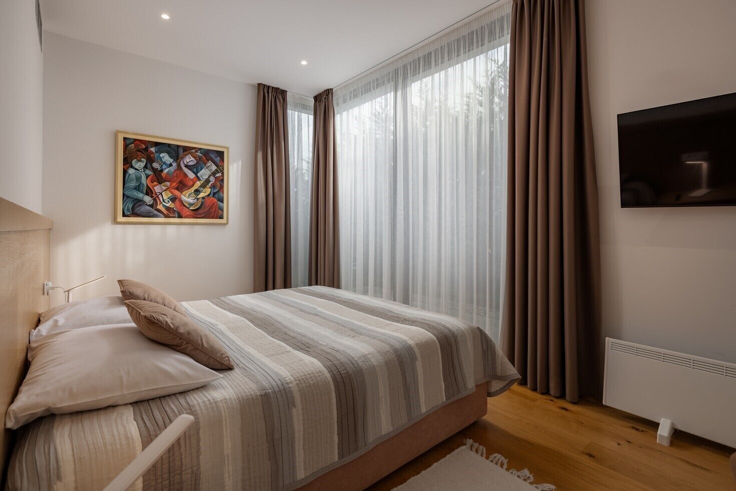 A bedroom with a bed, a painting, a TV, and a window with curtains.