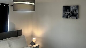 A modern bedroom with a large bed, a hanging lamp, a bedside table with a lamp, and a framed picture on the wall. - cozy serene flat (Dudley)