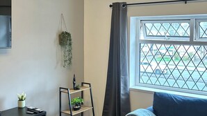 A modern living room with a black sofa, a white TV stand, a plant, a black shelving unit, and a window with a view of the street. - cozy serene flat (Dudley)