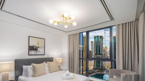Ein modernes Hotelzimmer mit einem großen Bett, Blick auf die Stadt und einem durch das Fenster sichtbaren Pool.
