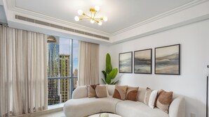 Ein modernes Wohnzimmer mit einer gebogenen Couch, einem großen Fenster mit Vorhängen, einer Deckenleuchte und gerahmten Kunstwerken an der Wand.