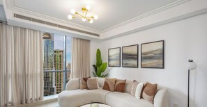Una sala de estar moderna con un sofá curvo, un ventanal con cortinas, una lámpara de techo y cuadros en la pared.