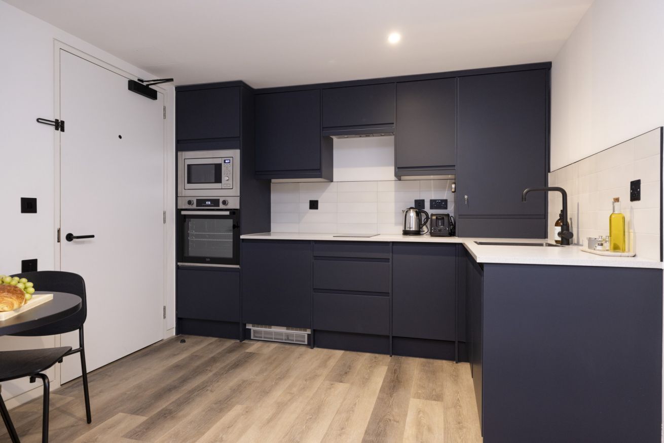Une cuisine moderne avec des meubles de couleur sombre, un plan de travail blanc, un four encastré et un four à micro-ondes.