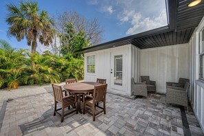 A patio with a round table and chairs, surrounded by a garden with palm trees and other greenery. - 3 min walk to beach/Heated Pool/Games/Kids area (Clearwater Beach)