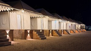 Une rangée de tentes, chacune accessible par quelques marches, est installée sur une plage de sable, la nuit.