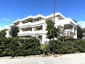 En flervåningsbostadsbyggnad med balkonger, omgiven av grönska.