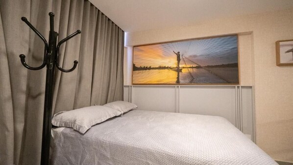 A hotel room with a bed, a coat rack, and a painting of a sunset over a bridge. - Flat 303-FM20 na praia de Cabo Branco (João Pessoa)
