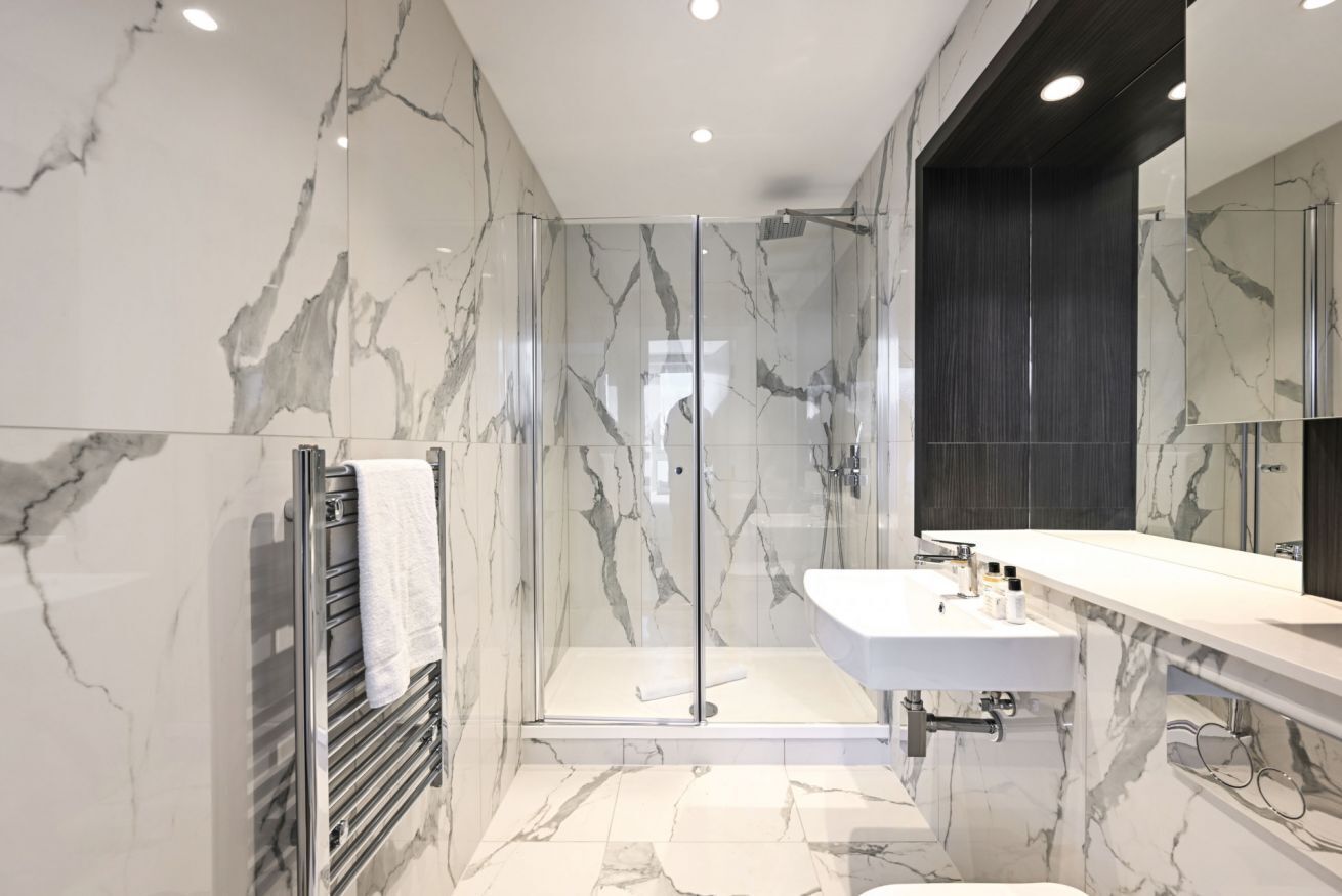A modern bathroom with a glass-enclosed shower, a white sink, and a large mirror.