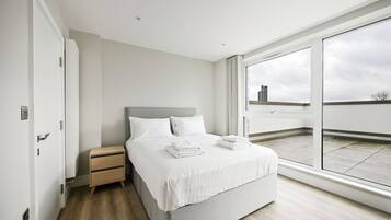 A modern bedroom with a large window, a bed, a nightstand, and a wooden floor.