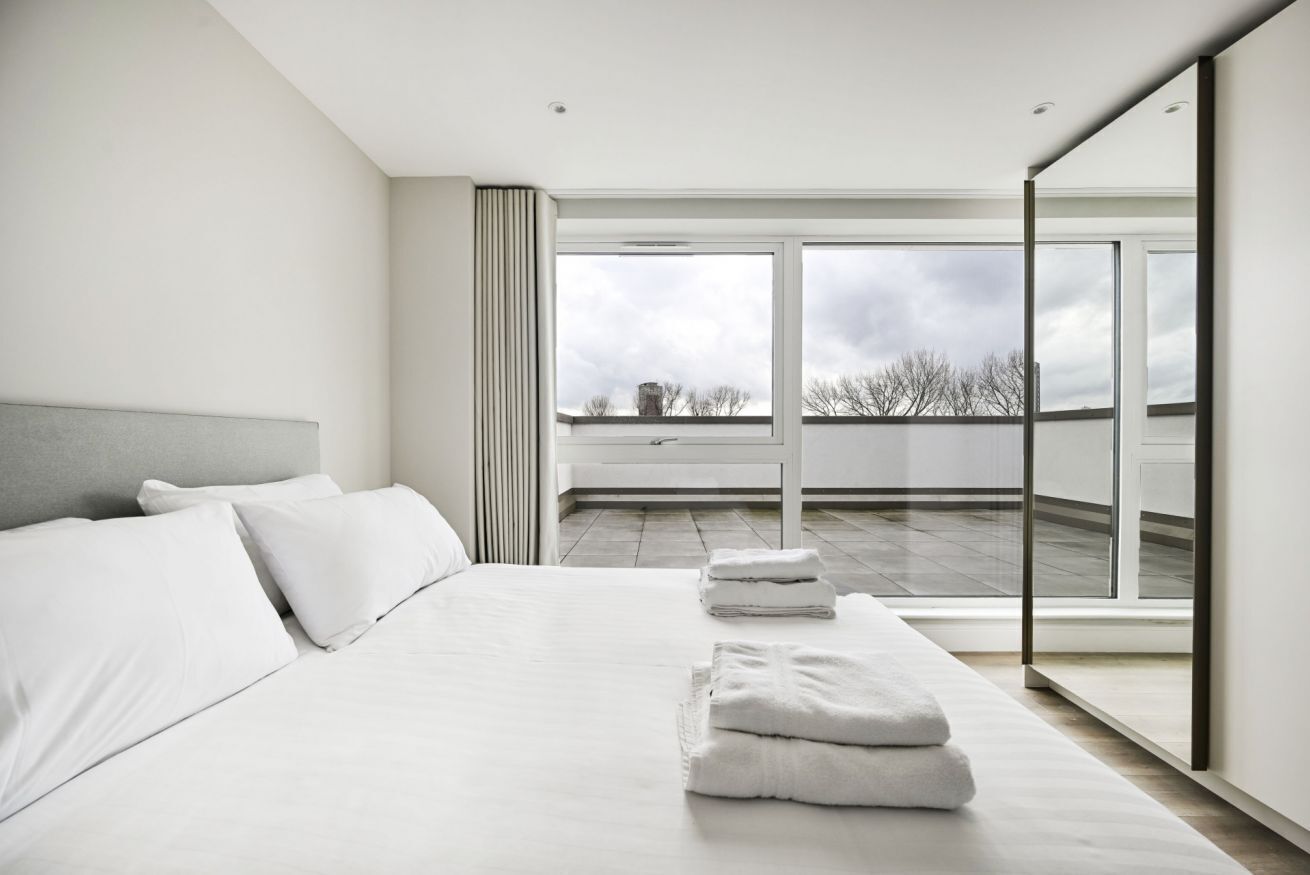 A modern bedroom with a large bed, a view of the sky, and a balcony.