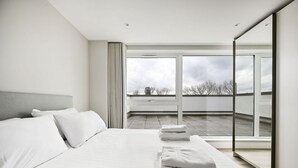 A modern bedroom with a large bed, a view of the sky, and a balcony. - Argyl | Modern 2 Bed Apt. with Balcony & Elevator (Greater London)