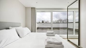 A modern bedroom with a large bed, a view of the sky, and a balcony.