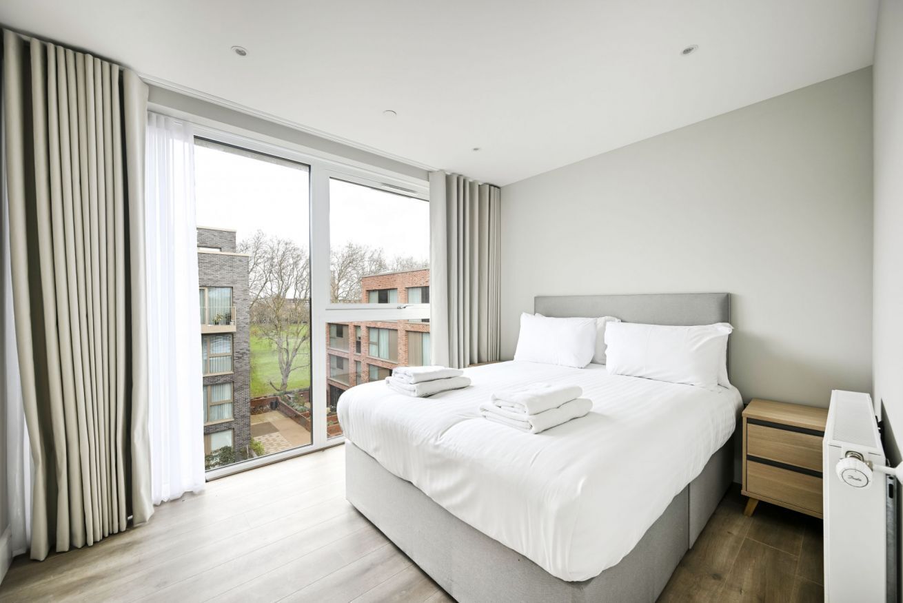 A modern hotel room with a large bed, a bedside table, and a view of the city.
