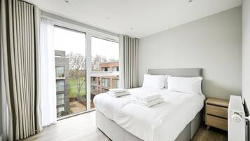 A modern hotel room with a large bed, a bedside table, and a view of the city.