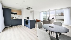 A modern kitchen with dark cabinets, a central island, and a dining area with a round table and chairs. - Argyl | Modern 2 Bed Apt. with Balcony & Elevator (Greater London)