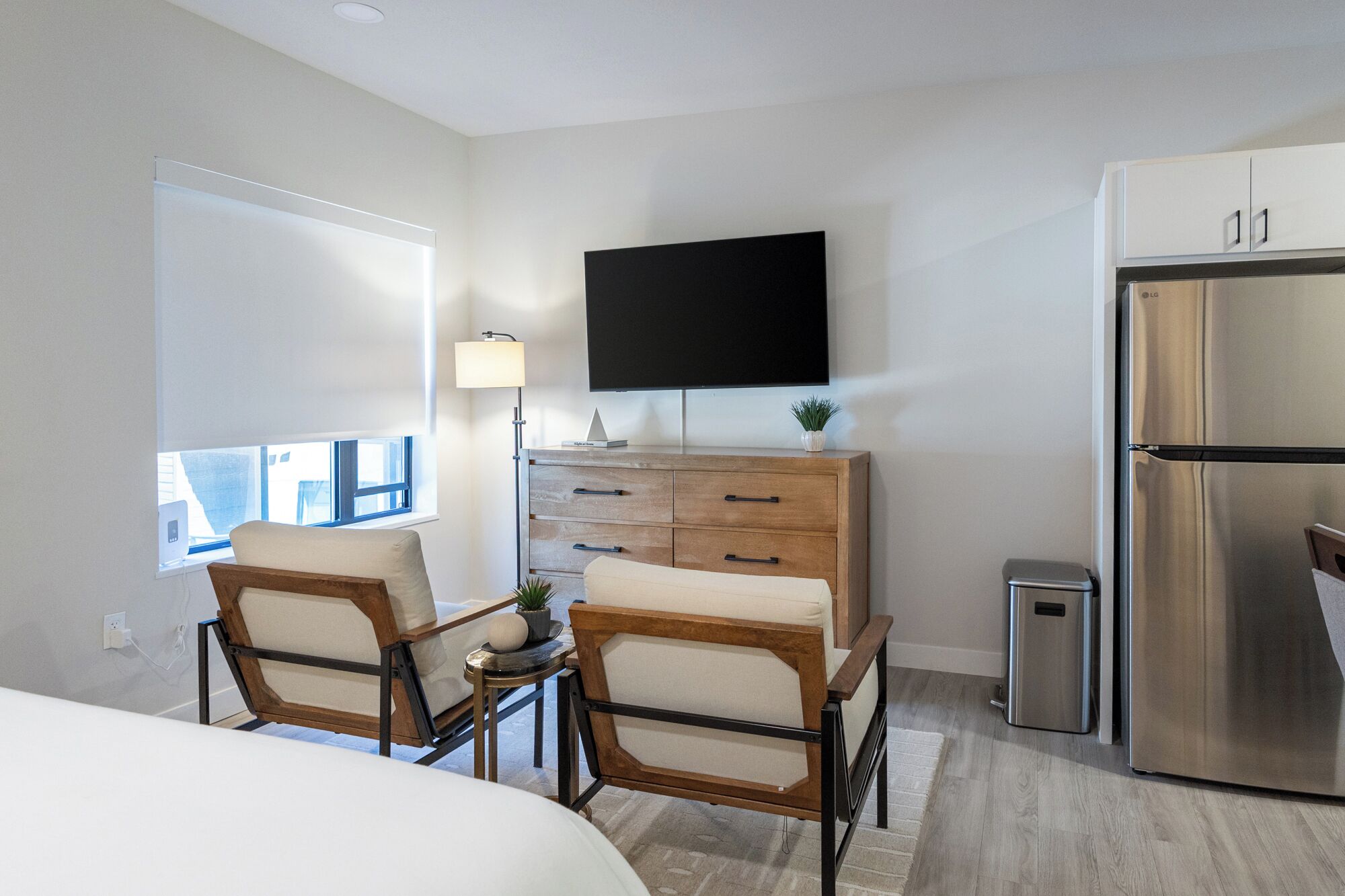 Camera d'albergo moderna con un letto, una piccola scrivania con una sedia, una TV a schermo piatto montata a parete, un settimino in legno, un frigorifero in acciaio inossidabile e una finestra con vista.