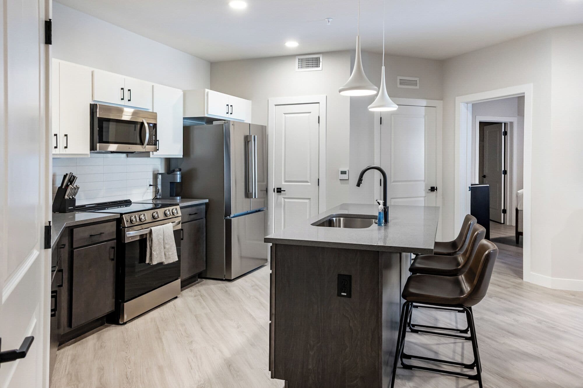 A modern kitchen with stainless steel appliances, a central island with bar stools, and a pendant light.