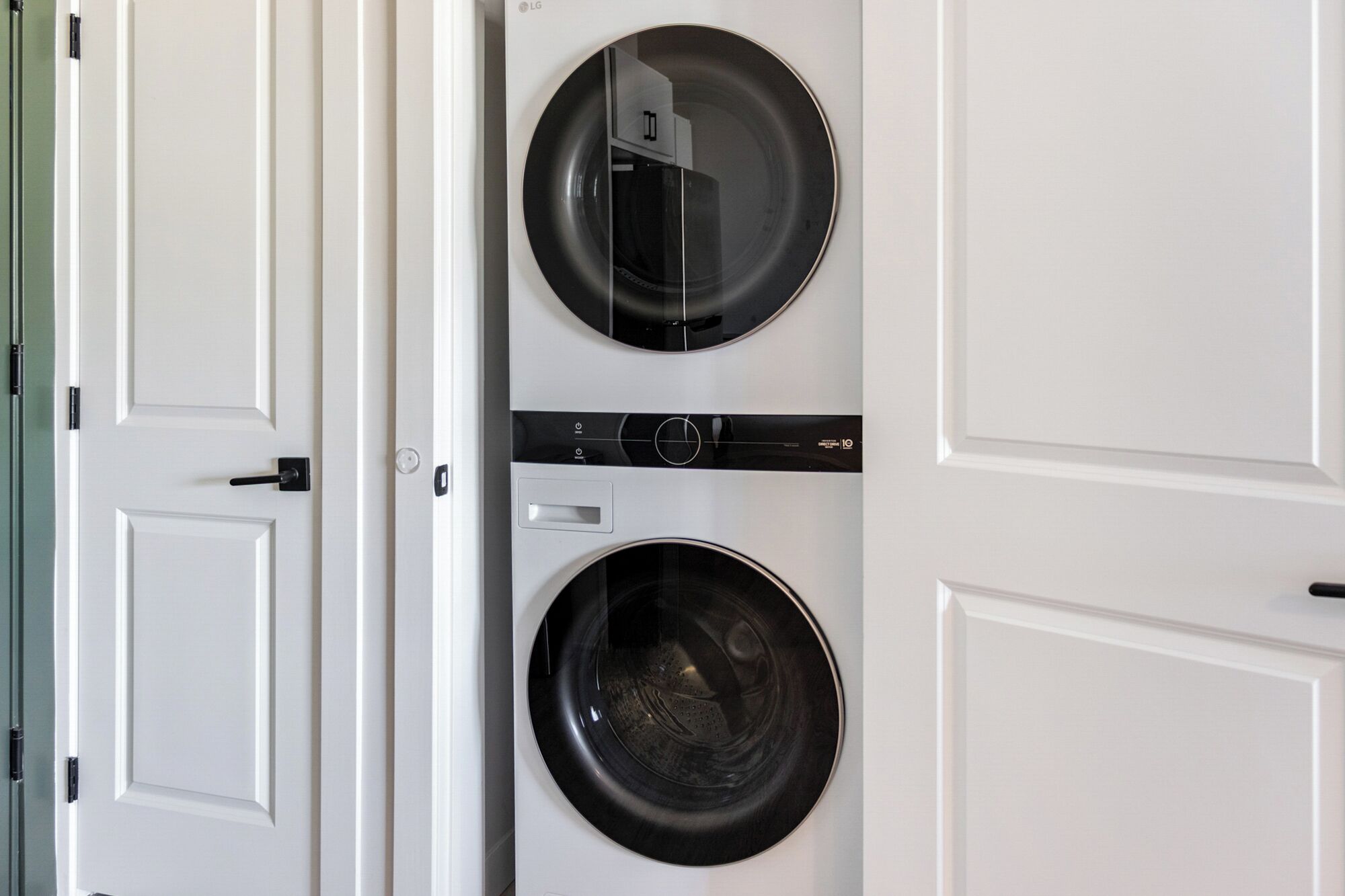 A front view of a laundry room with two washing machines and a dryer, white doors, and a glass door.