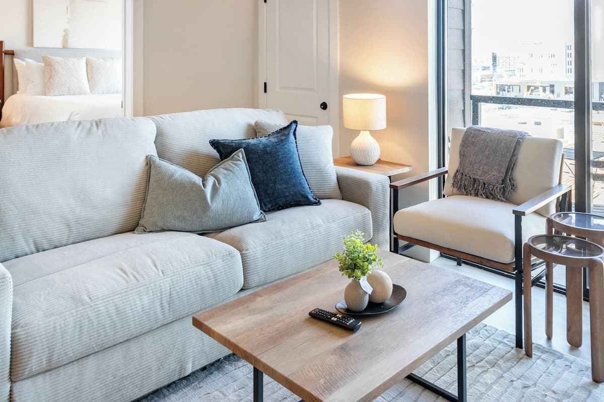 Ein modernes Wohnzimmer mit Sofa, Sessel, Couchtisch, Lampe und Blick auf die Stadt.