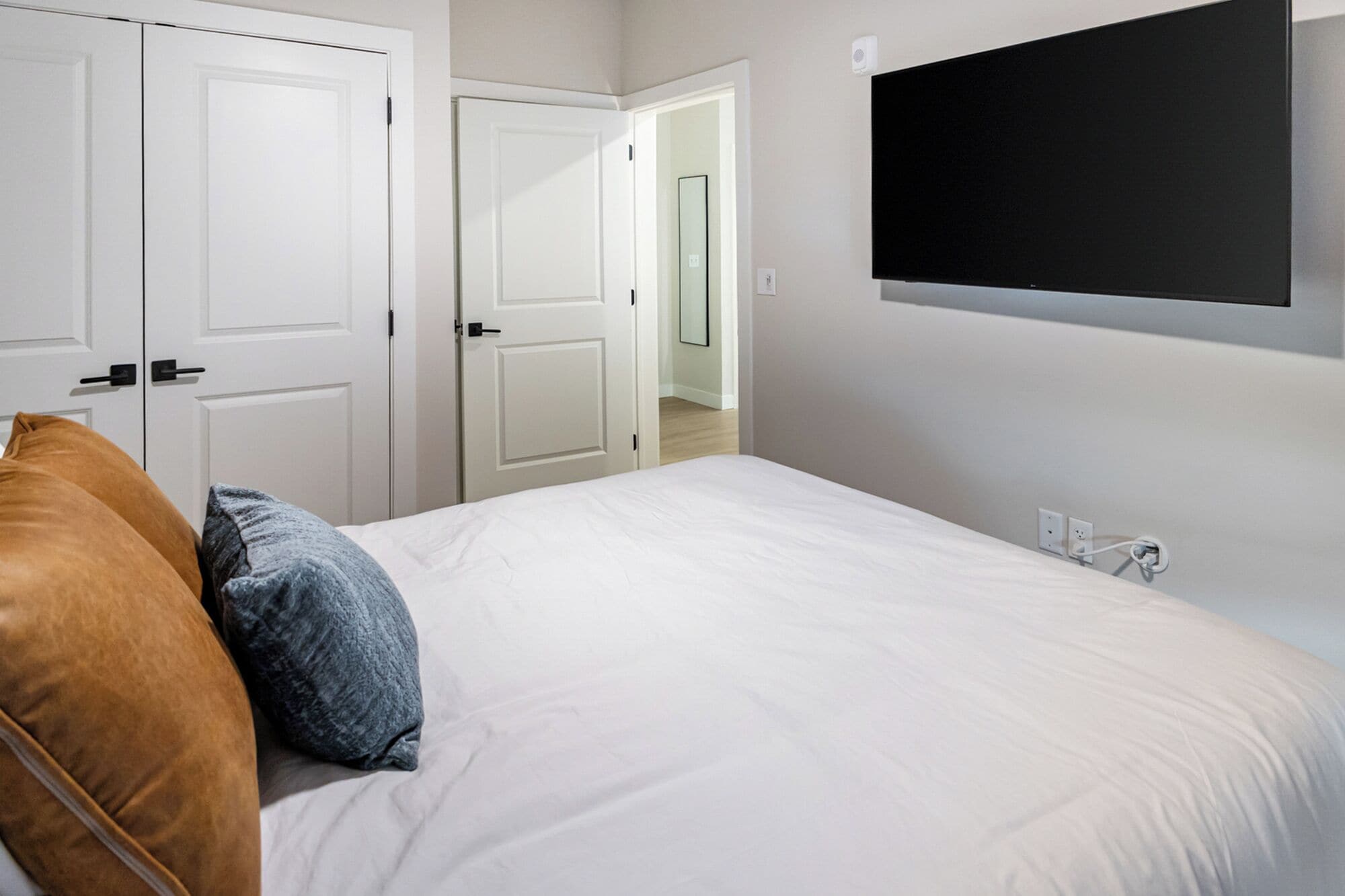 Un dormitori amb un llit, dos almoinos, una televisió penjada a la paret i una porta que dona a una altra habitació.