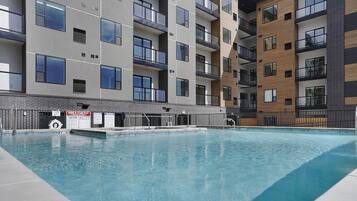 A modern building with a swimming pool, balconies, and a sign indicating no lifeguards on duty.
