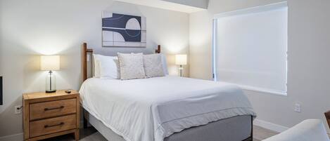 Un dormitorio con cama, mesitas de noche, ventilador de techo, una obra de arte en la pared y ventana con persianas.