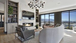 Ein modernes Wohnzimmer mit Kamin, einem großen Fenster mit Blick auf die Stadt und einer hohen Decke mit einem besonderen Kronleuchter.