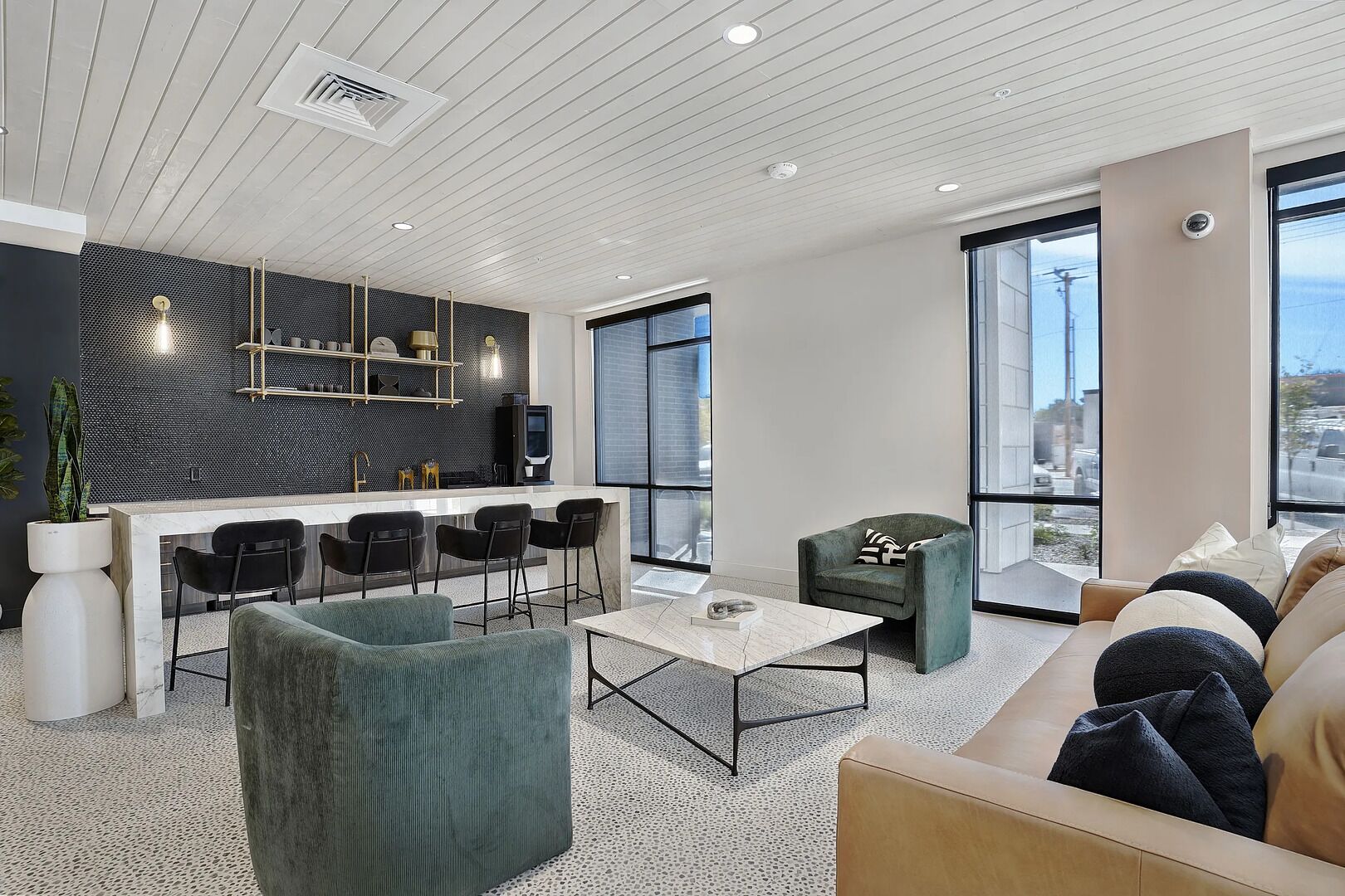 A modern kitchen with a bar area, a seating area with a sofa and chairs, and large windows offering a view.