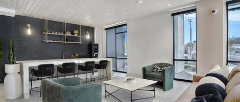 A modern kitchen with a bar area, a seating area with a sofa and chairs, and large windows offering a view.