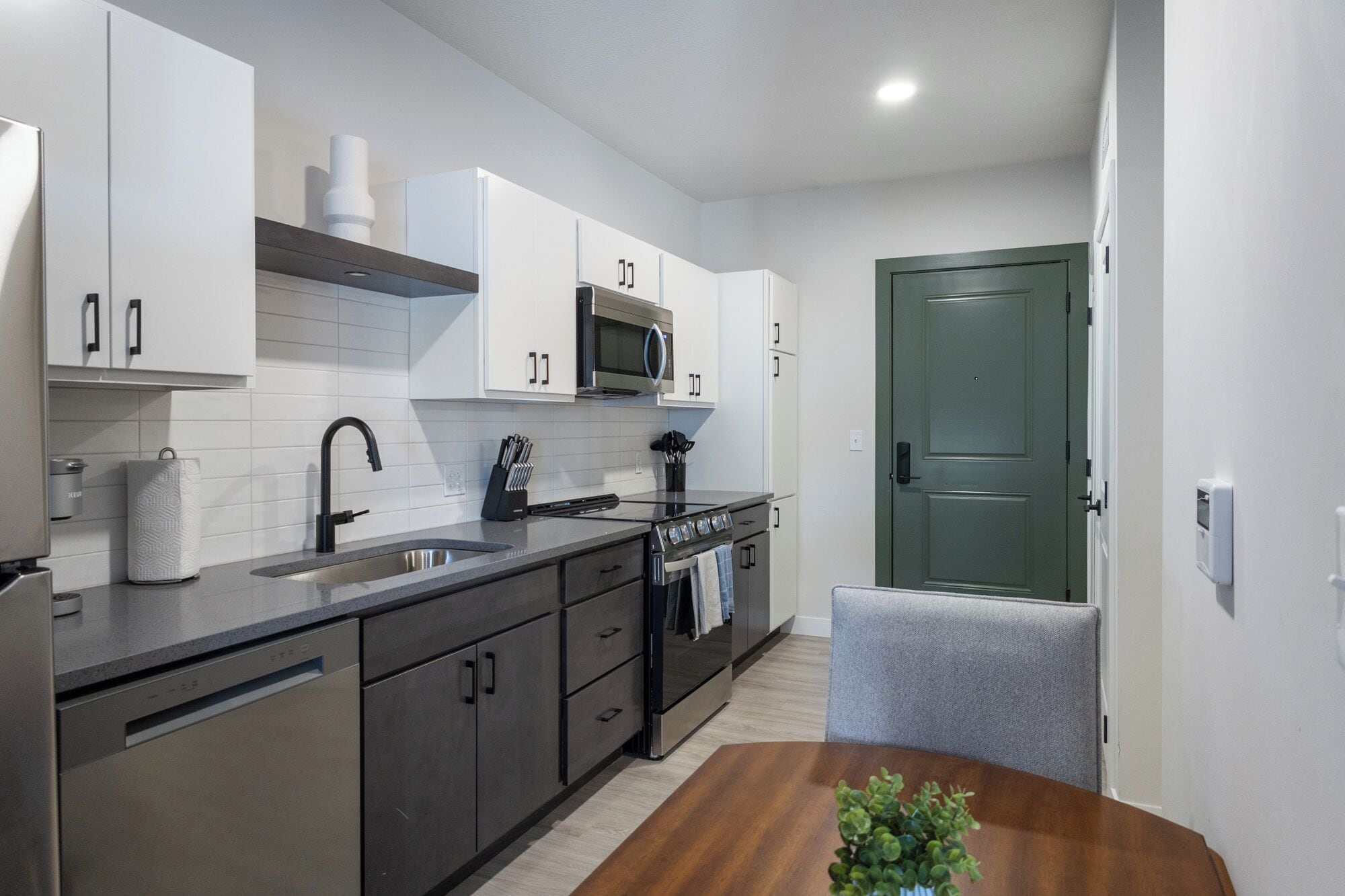 A modern kitchen with stainless steel appliances, white cabinetry, and a wooden dining table.