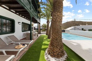 Ein Poolbereich mit Liegestühlen, einer Palme und einem Gebäude mit einem grünen Balkon.