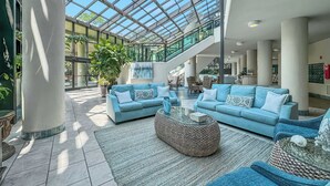 Spaziosa hall con soffitto alto e pannelli di vetro, caratterizzata da due divani azzurri, un tavolino da caffè intrecciato e una scala che conduce ai piani superiori.